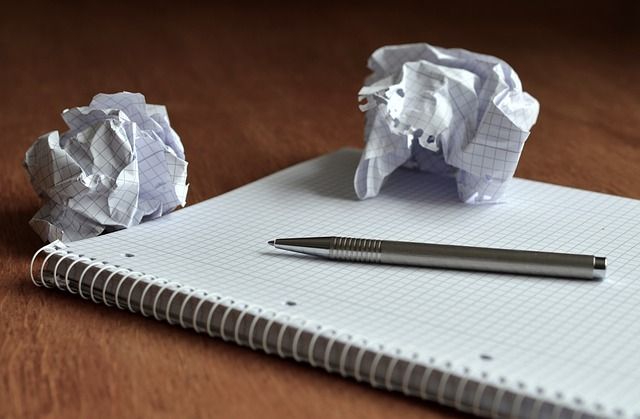 libreta con hoja en blanco, bolígrafo y papeles arrugados producto del perfeccionismo