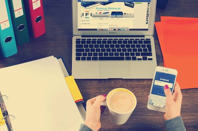 persona con ordenador y café mientras consulta redes sociales con su Mobil